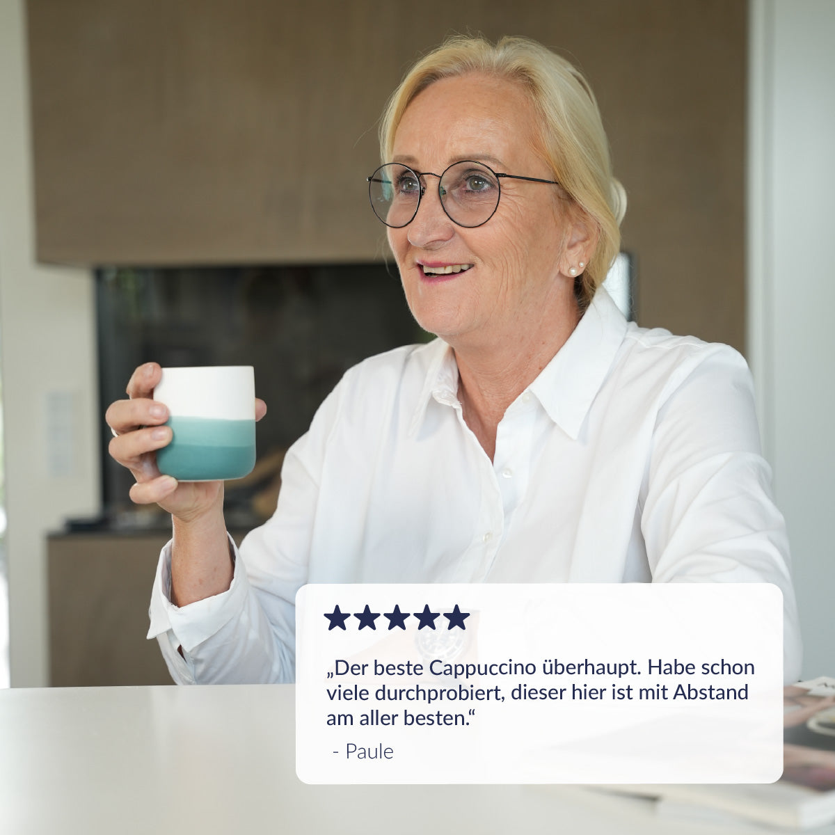 Frau hält einen blauen Porzellan Becher in der hand un dlächelt mit einem Kommentar zum cappuccino 